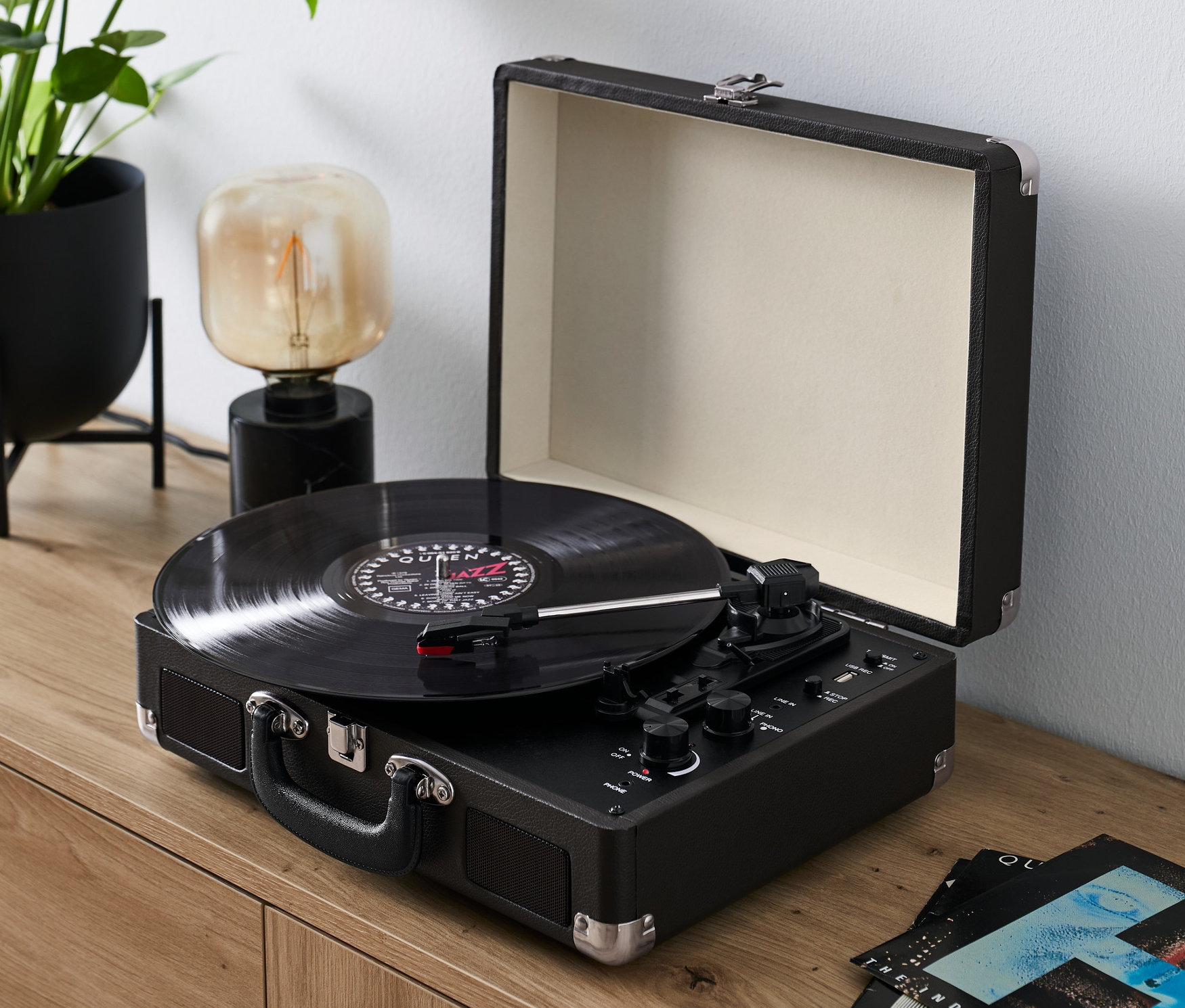 Czarny, przenośny gramofon retro z Bluetooth odtwarza płytę na drewnianej komodzie.