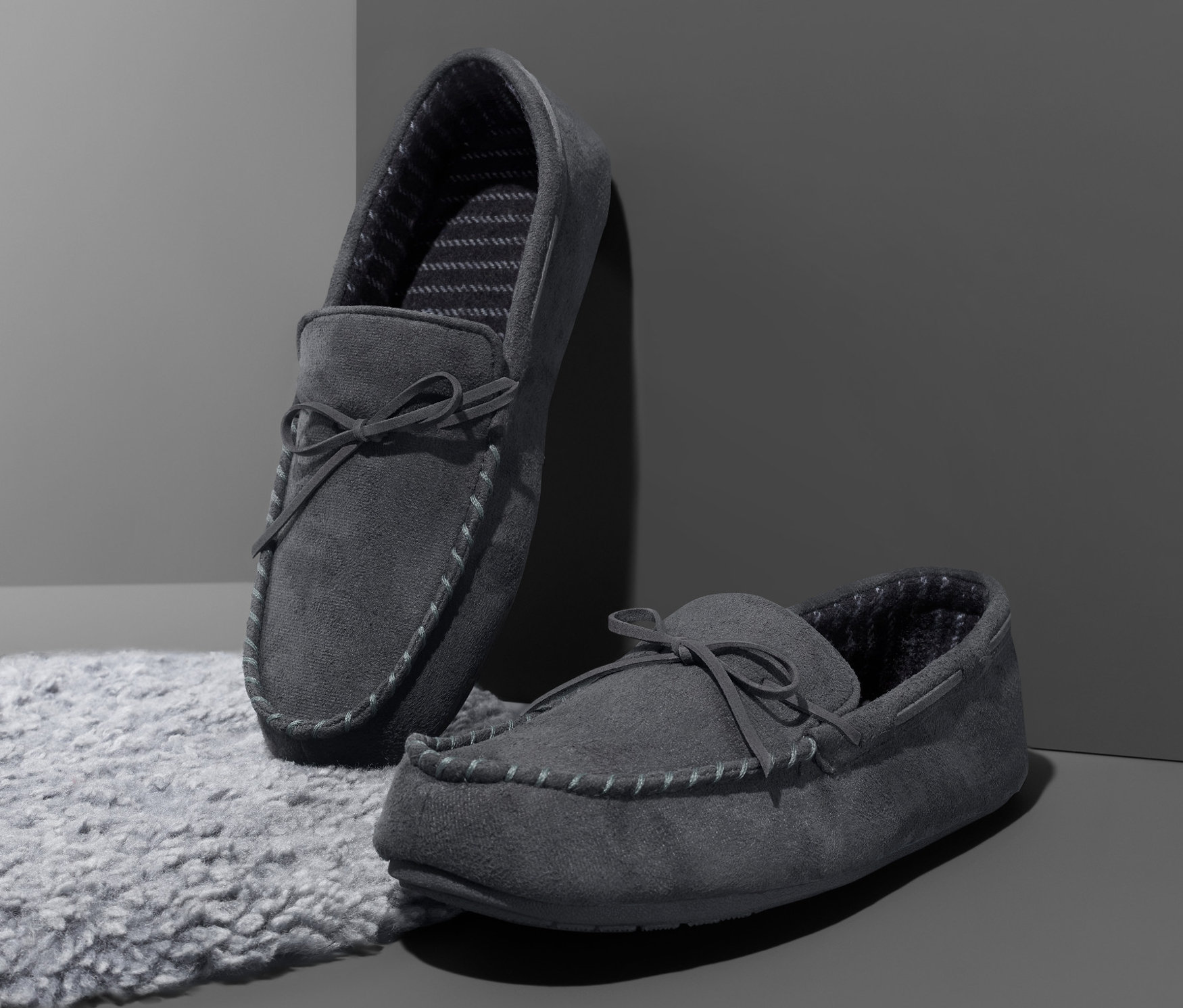 Dwa szare męskie kapcie stoją na szarym dywanie przed szarą ścianą.