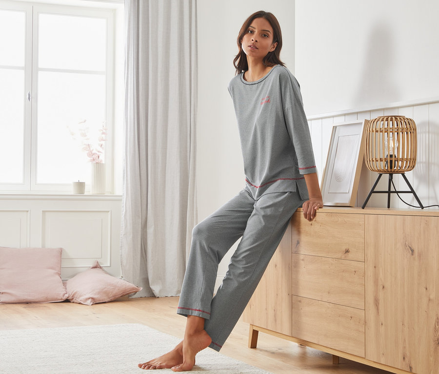 Kobieta siedzi na komodzie w szarej piżamie w delikatne paski.