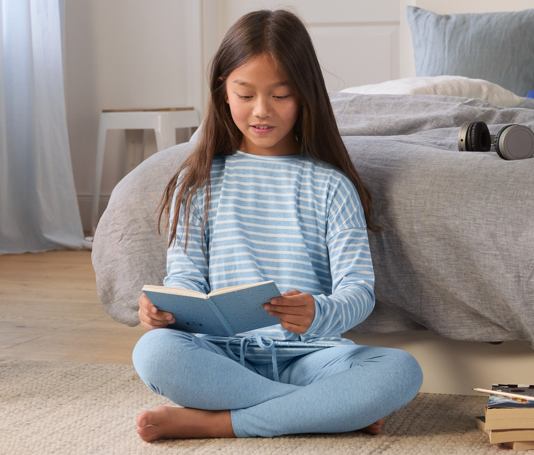 Dziewczyna siedzi na podłodze i czyta książkę. Ma na sobie błękitną piżamę dziewczęcą.