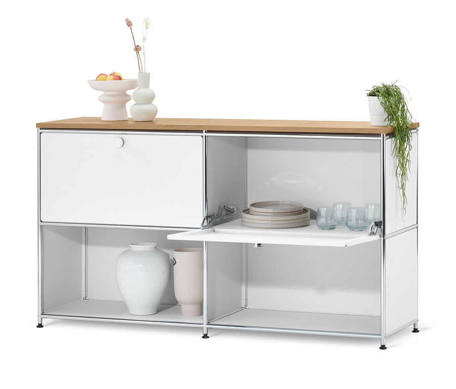 Biała szafka metalowa typu sideboard "CN3" z drewnianym blatem i klapami. Na szafce wazon, owoce i kwiat.