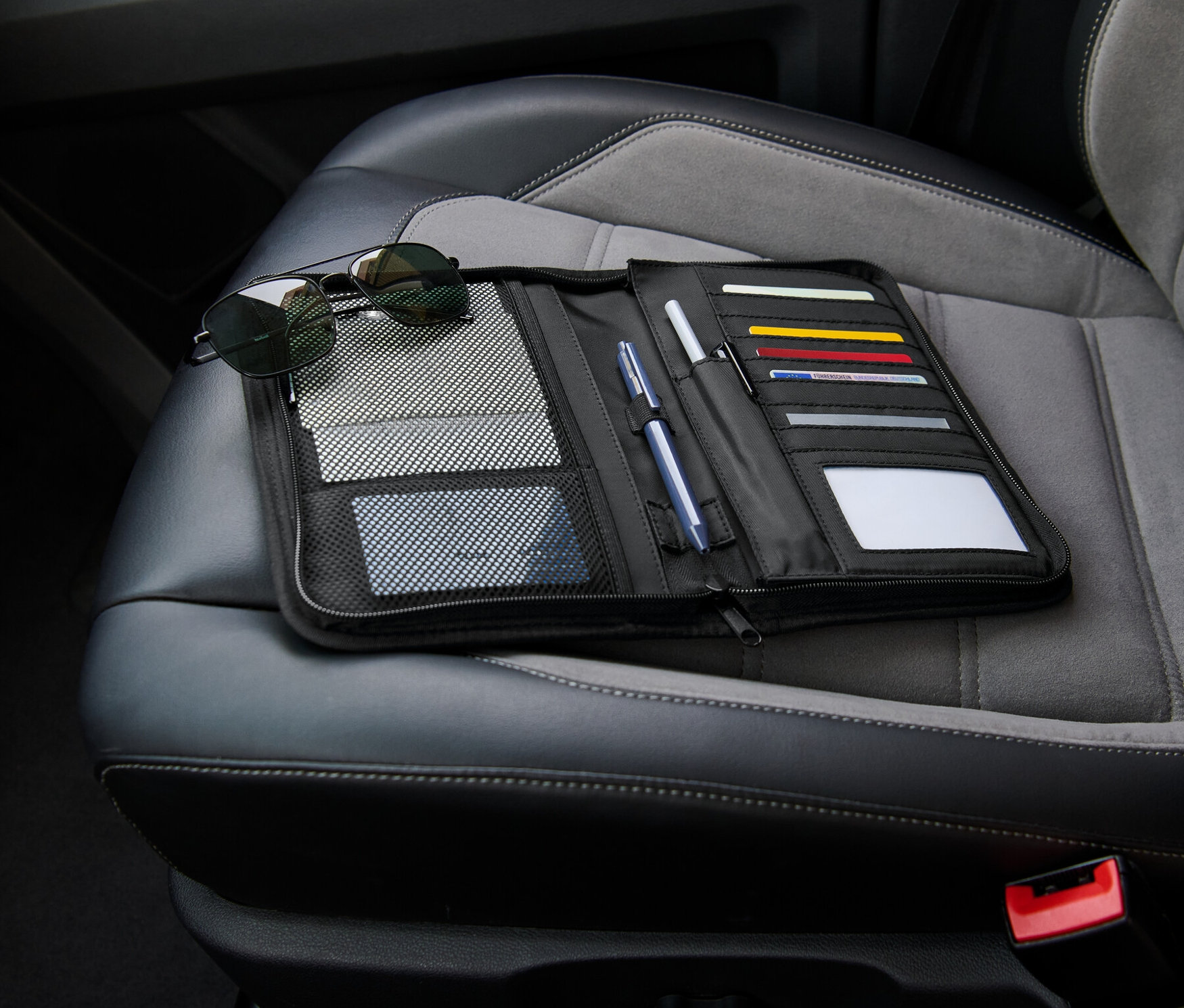 Czarny organizer do schowka na rękawiczki leży otwarty na siedzeniu samochodu obok okularów przeciwsłonecznych.