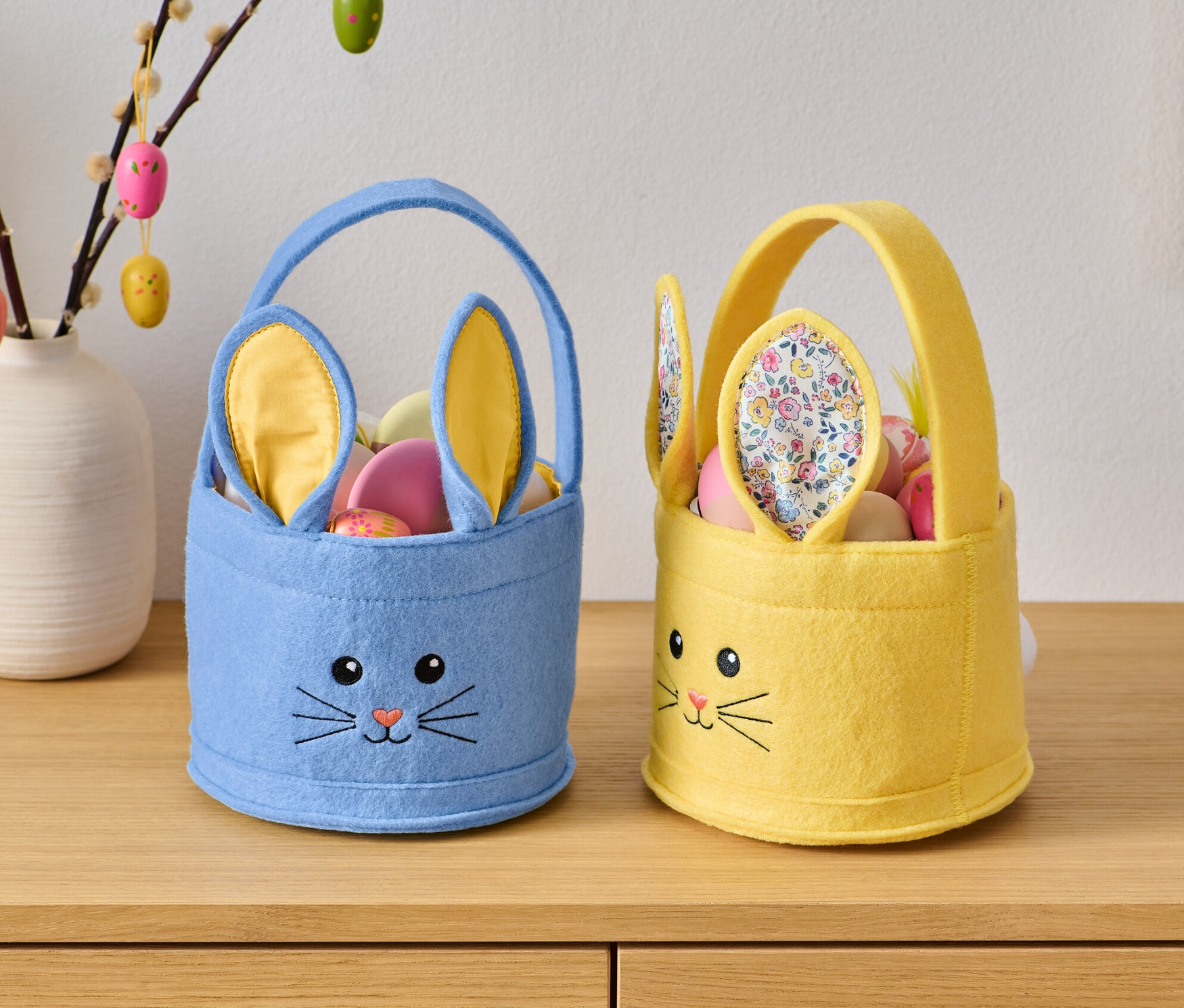 Dwa koszyczki wielkanocne z króliczą twarzą stoją na drewnianej komodzie.
