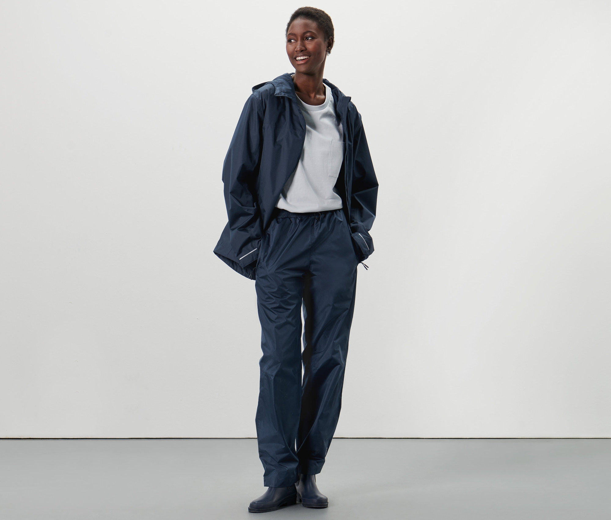 Afroamerykanka stoi i ma na sobie unisexowe spodnie przeciwdeszczowe i kurtkę przeciwdeszczową.