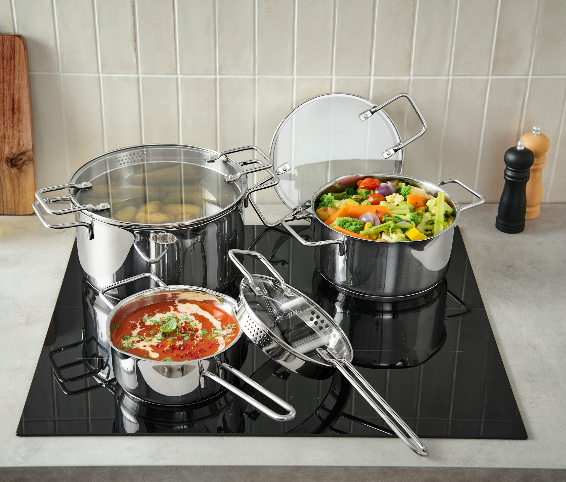 Trzy profesjonalne garnki ze stali nierdzewnej stoją na czarnej płycie grzejnej, jeden garnek jest pełen ziemniaków, drugi warzyw, a trzeci sosu pomidorowego.