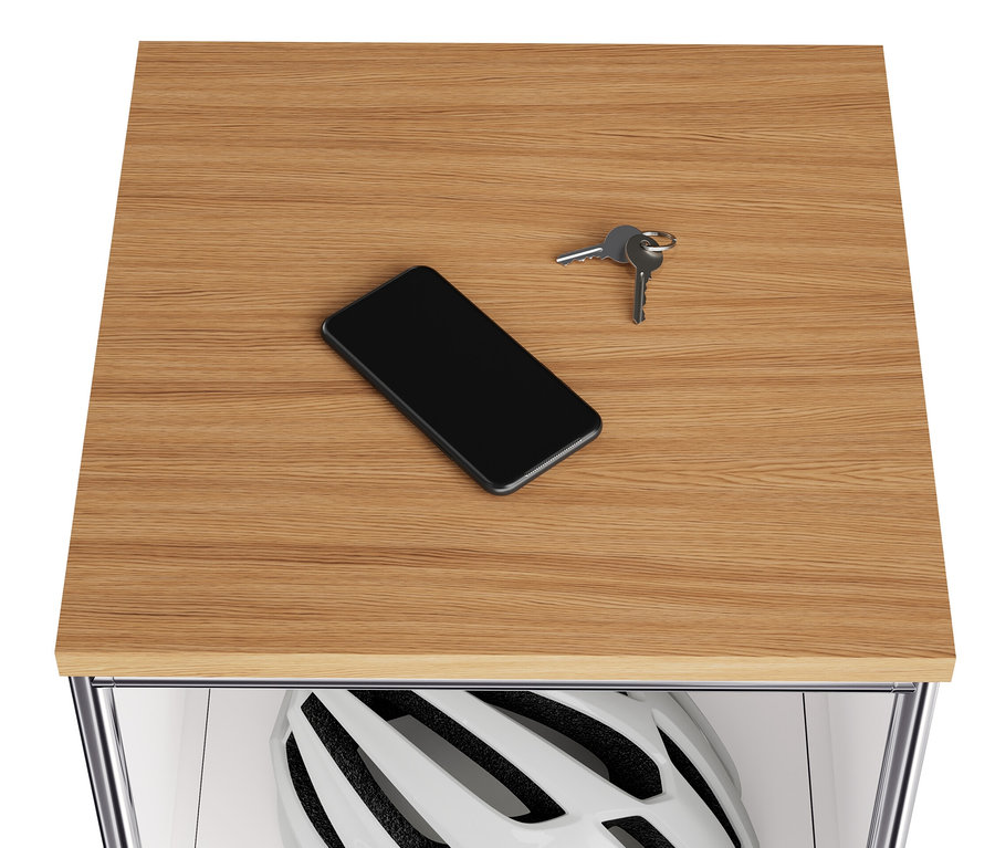 Na drewnianym blacie wąskiej, białej metalowej komody „CN3” leżą telefon komórkowy i klucze. W uchylnej komorze znajduje się kask.