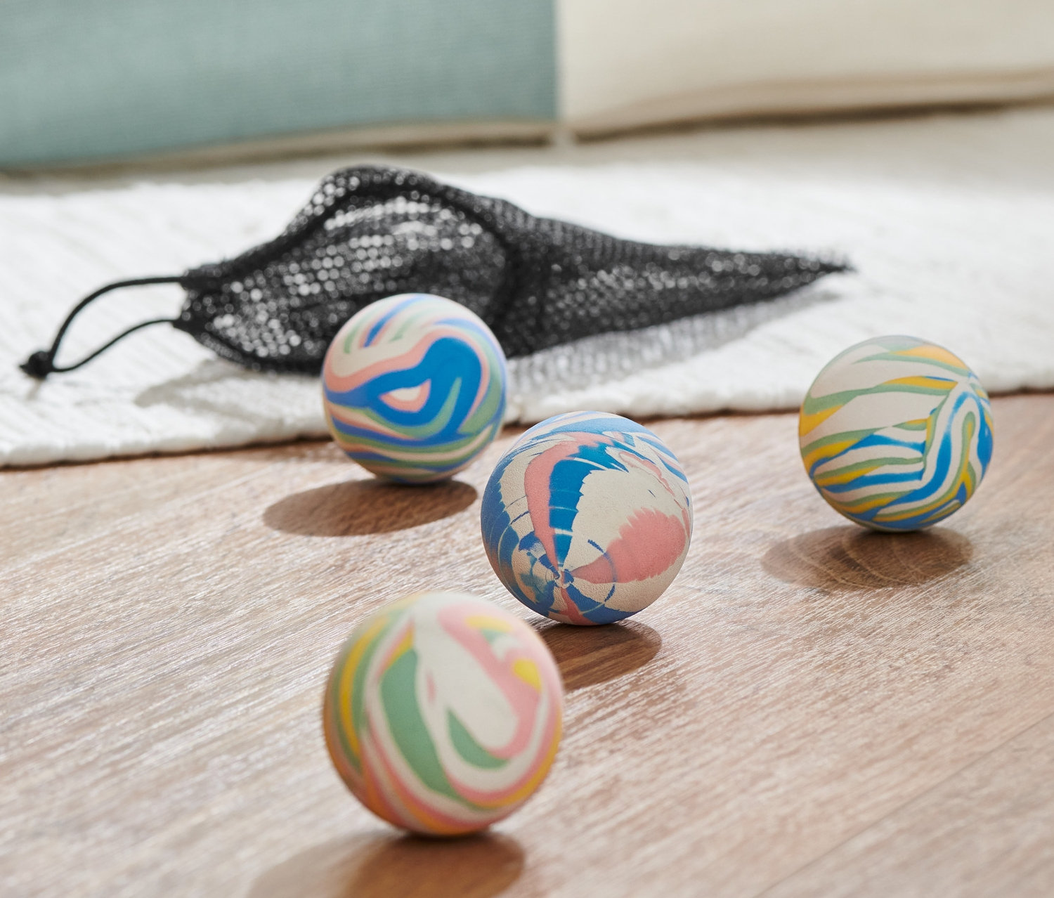 Cztery wielokolorowe piłeczki kangurki i czarna siatkowa torba na drewnianej podłodze.