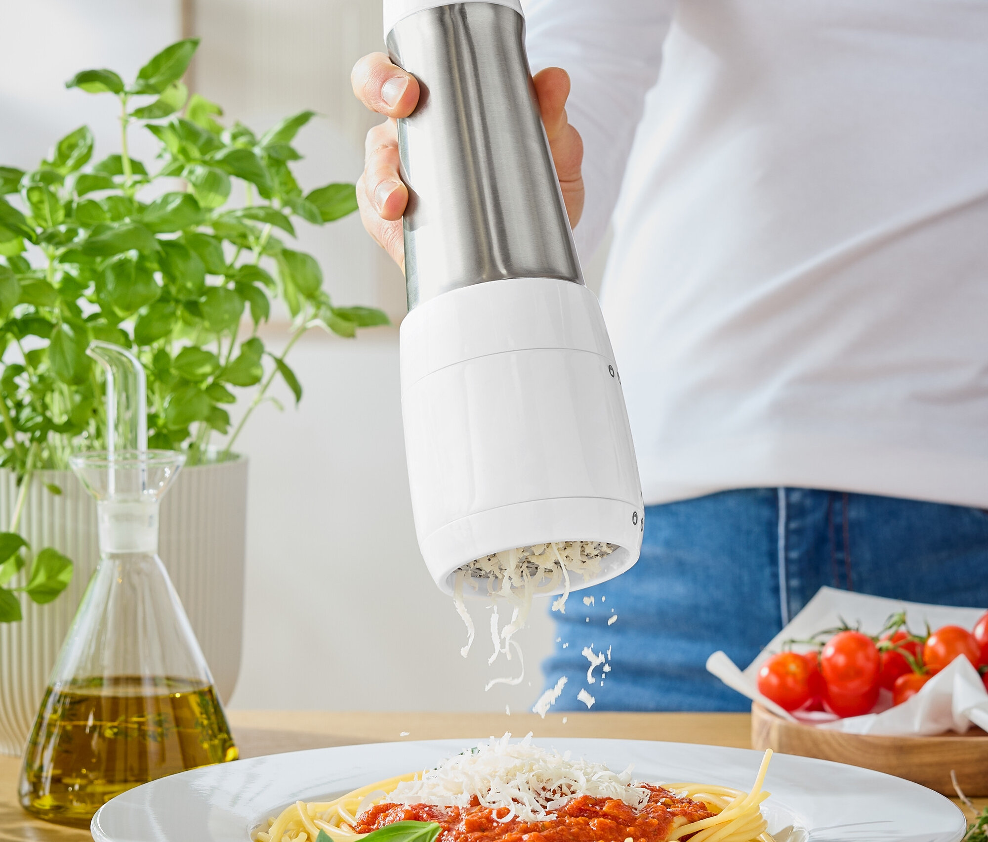 Kobieta trze ser na spaghetti z sosem pomidorowym za pomocą młynka do sera.