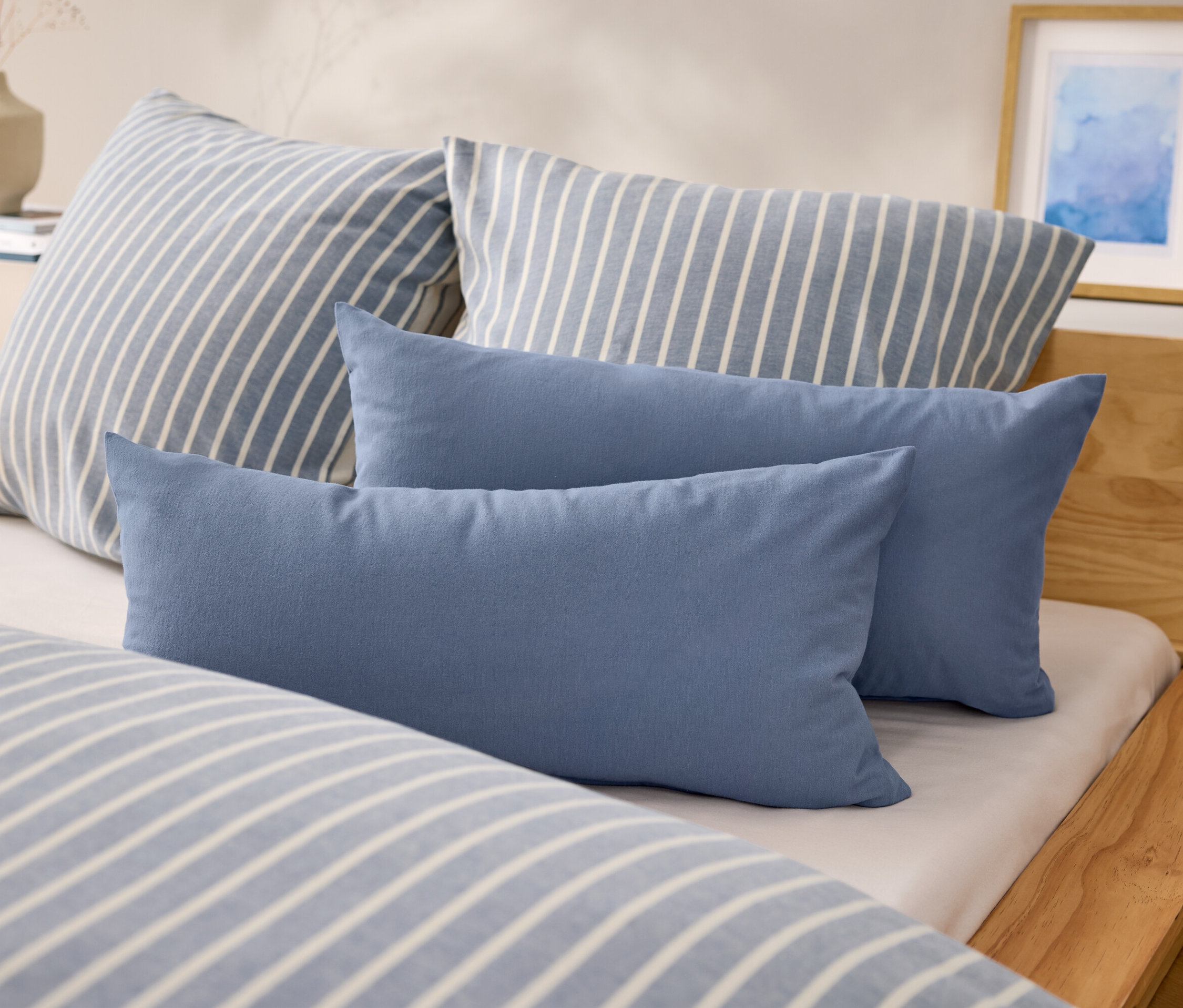 Na łóżku leżą dwie niebieskie, prostokątne poduszki i dwie poduszki w niebiesko-białe paski.