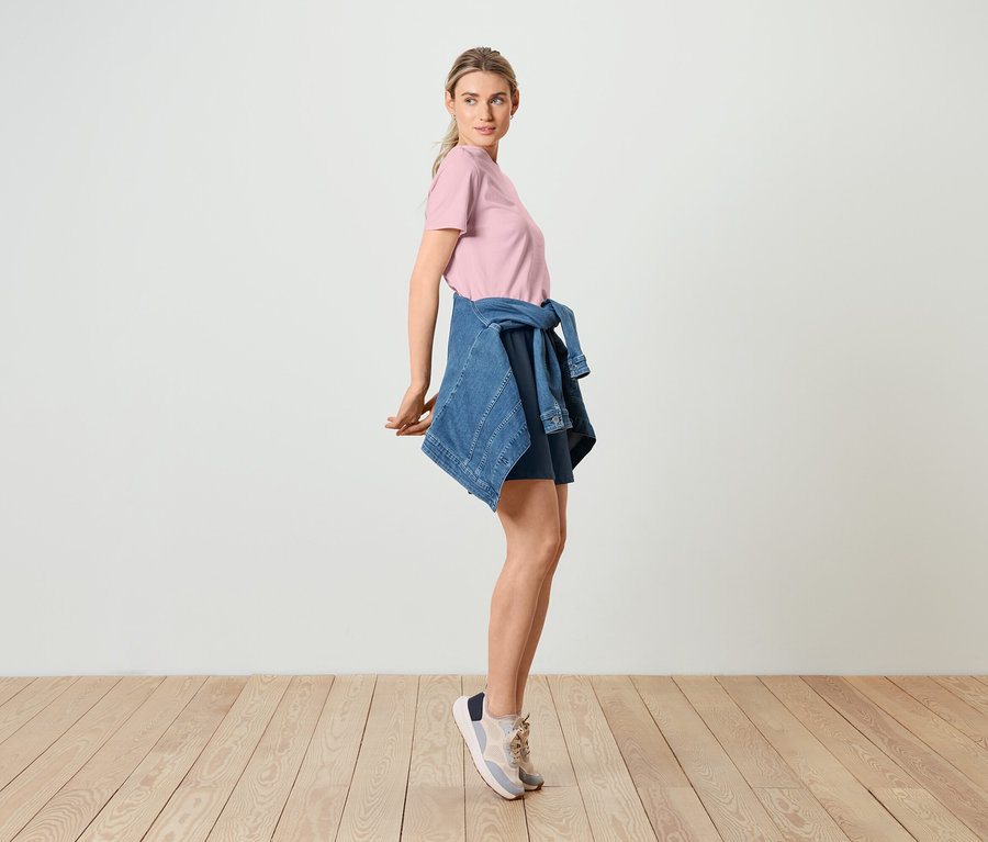 Kobieta pozuje w różowej koszulce, kurtce dżinsowej i dresowych szortach.