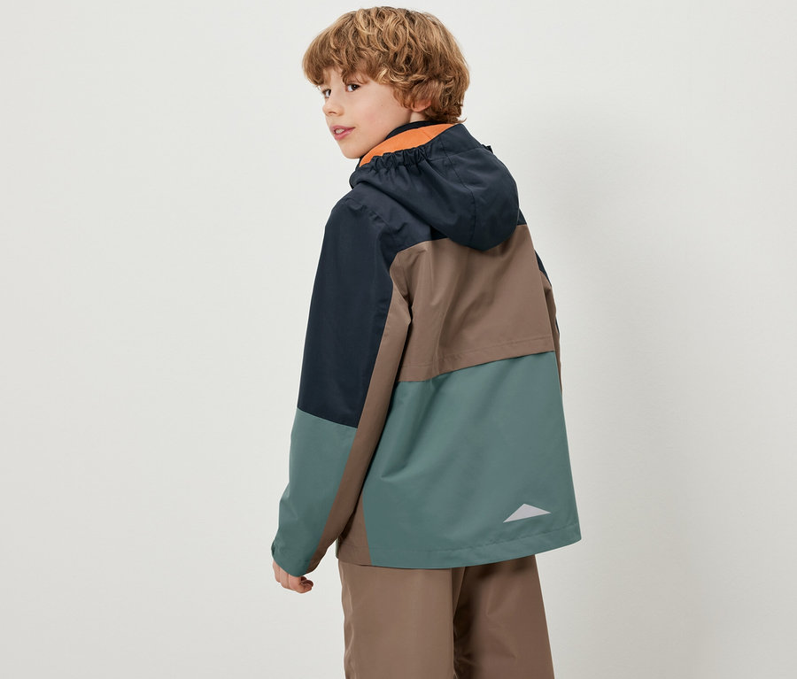 Chłopiec spogląda przez ramię, ubrany w kolorową dziecięcą kurtkę na każdą pogodę.