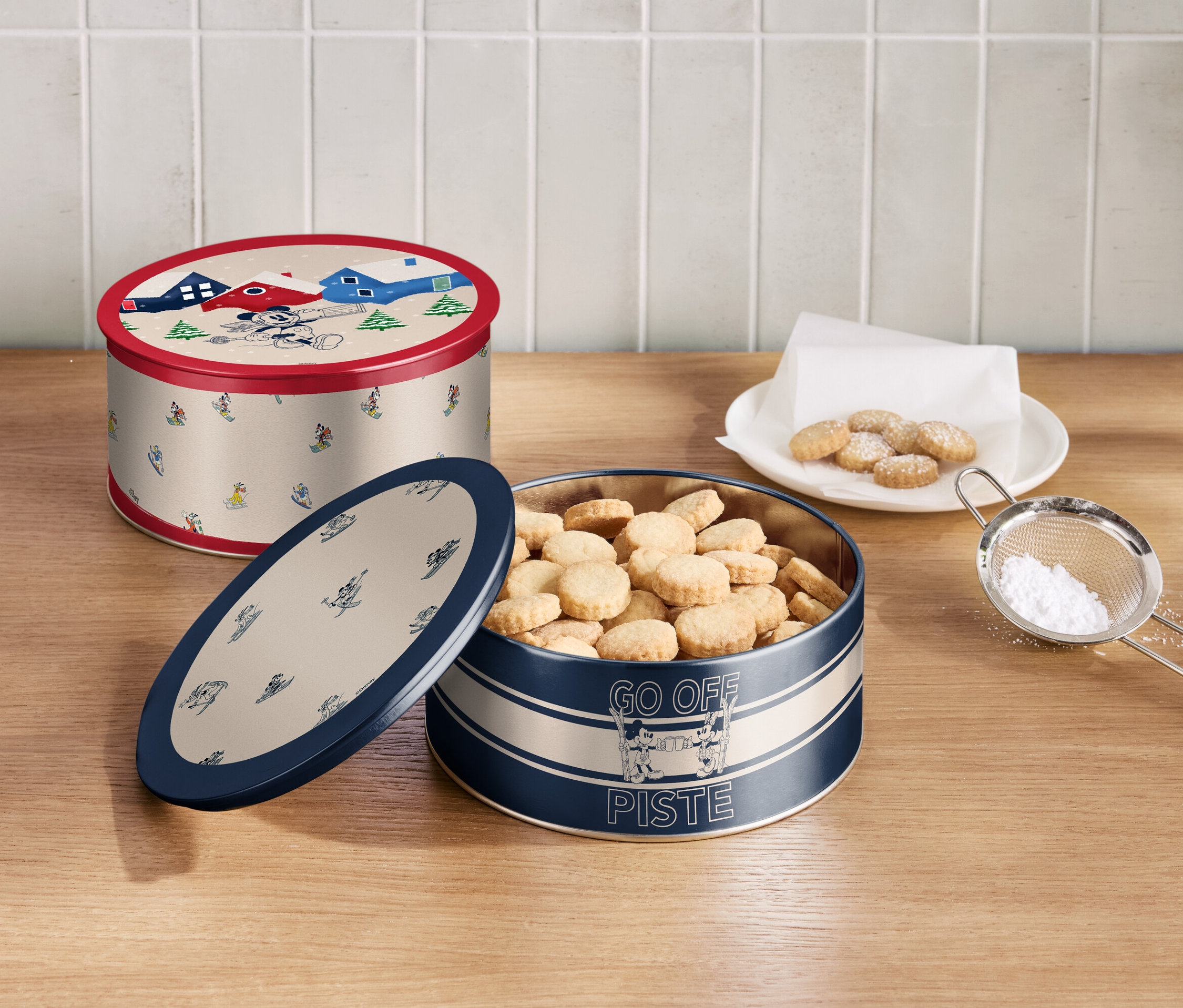 Dwie puszki z ciasteczkami i sitko z cukrem pudrem na drewnianym stole.