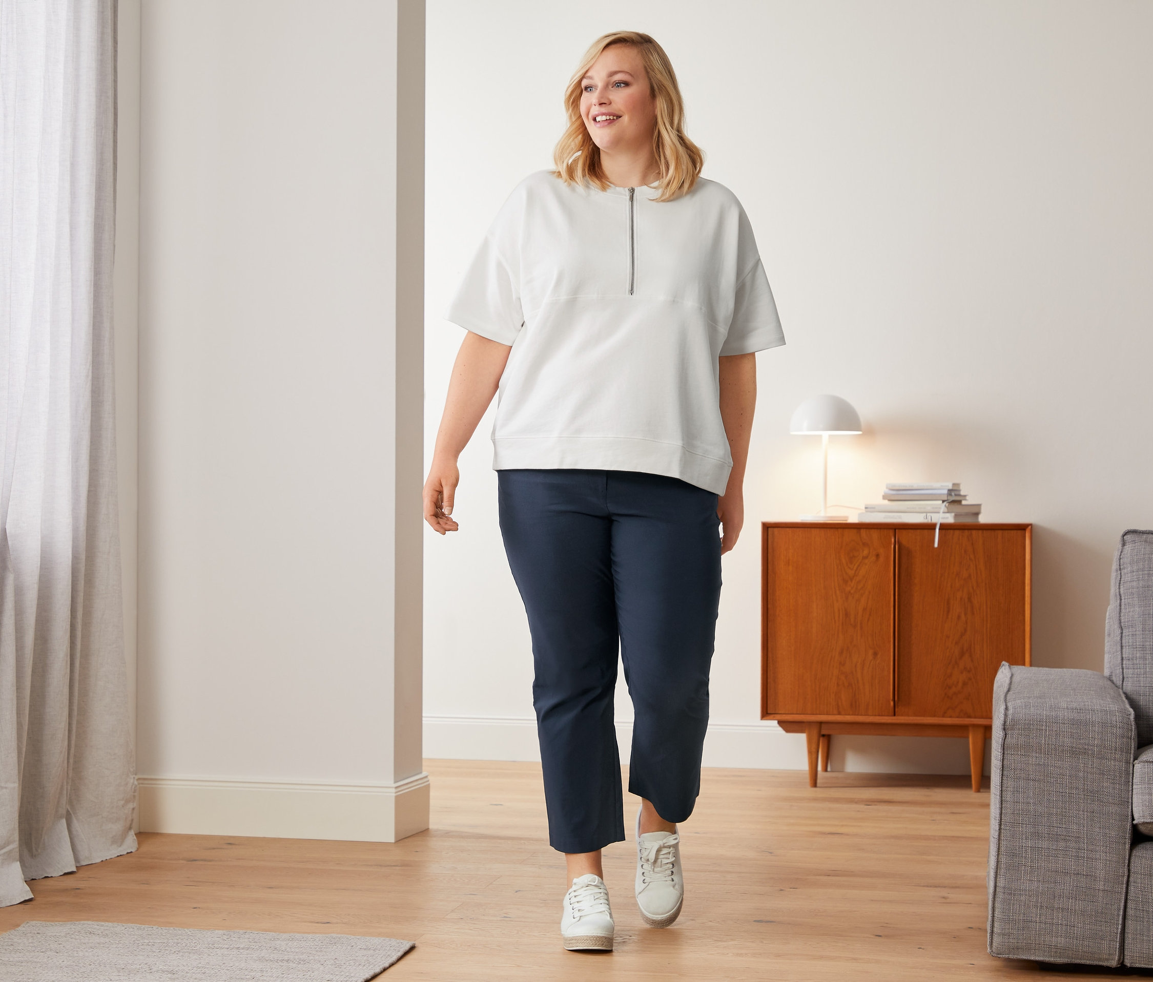 Kobieta idzie w białych płóciennych butach sportowych, białych spodniach stretchowych o długości 7/8 i bluzie oversized.