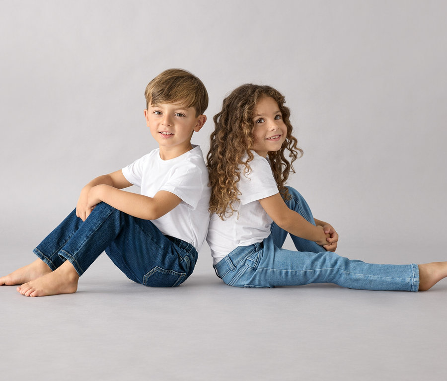 Chłopiec i dziewczynka siedzą do siebie plecami, oboje w białych T-shirtach i spodniach na gumce – fason „Luca”.