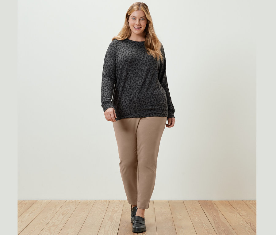 Kobieta idzie, ma na sobie wzorzystą bluzkę z rękawami typu nietoperz i beżowe spodnie dresowe.