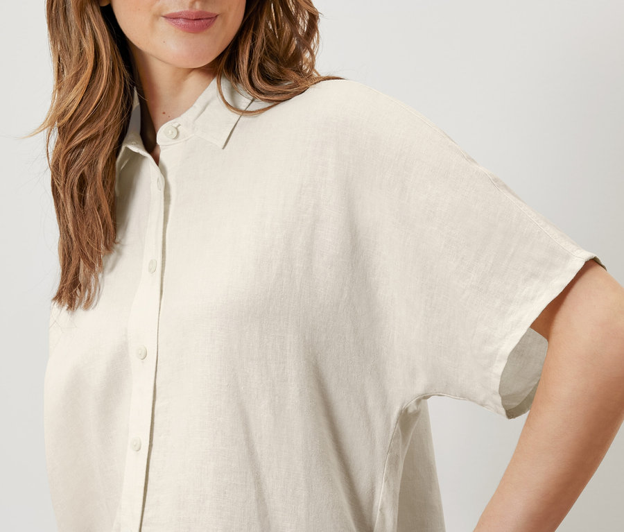 Kobieta ma na sobie lnianą bluzkę w kolorze kremowym.