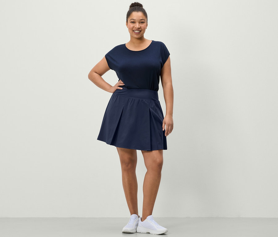 Kobieta pozuje w granatowej spódnicy sportowej i granatowej koszulce sportowej.