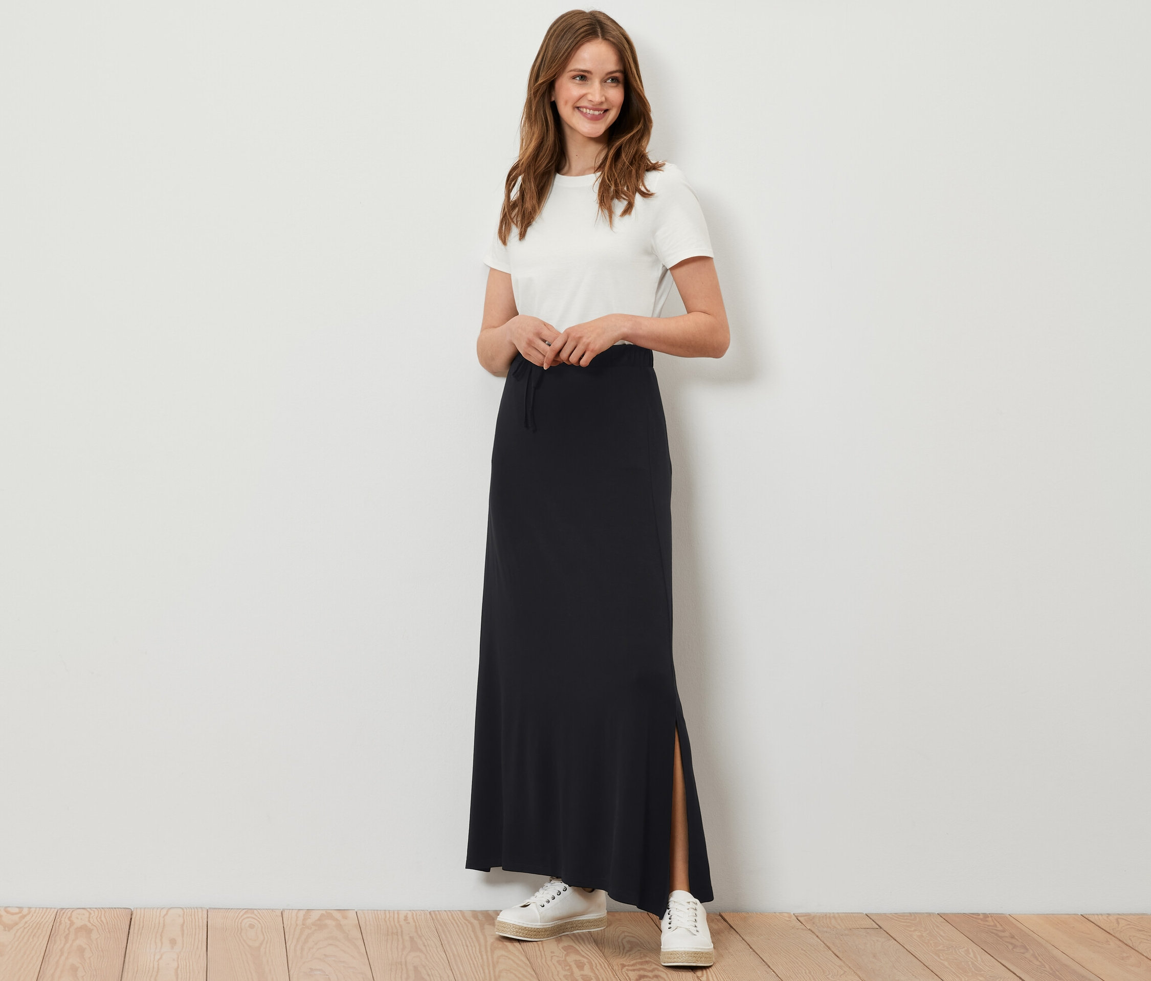 Kobieta pozuje w długiej czarnej spódnicy dżersejowej.