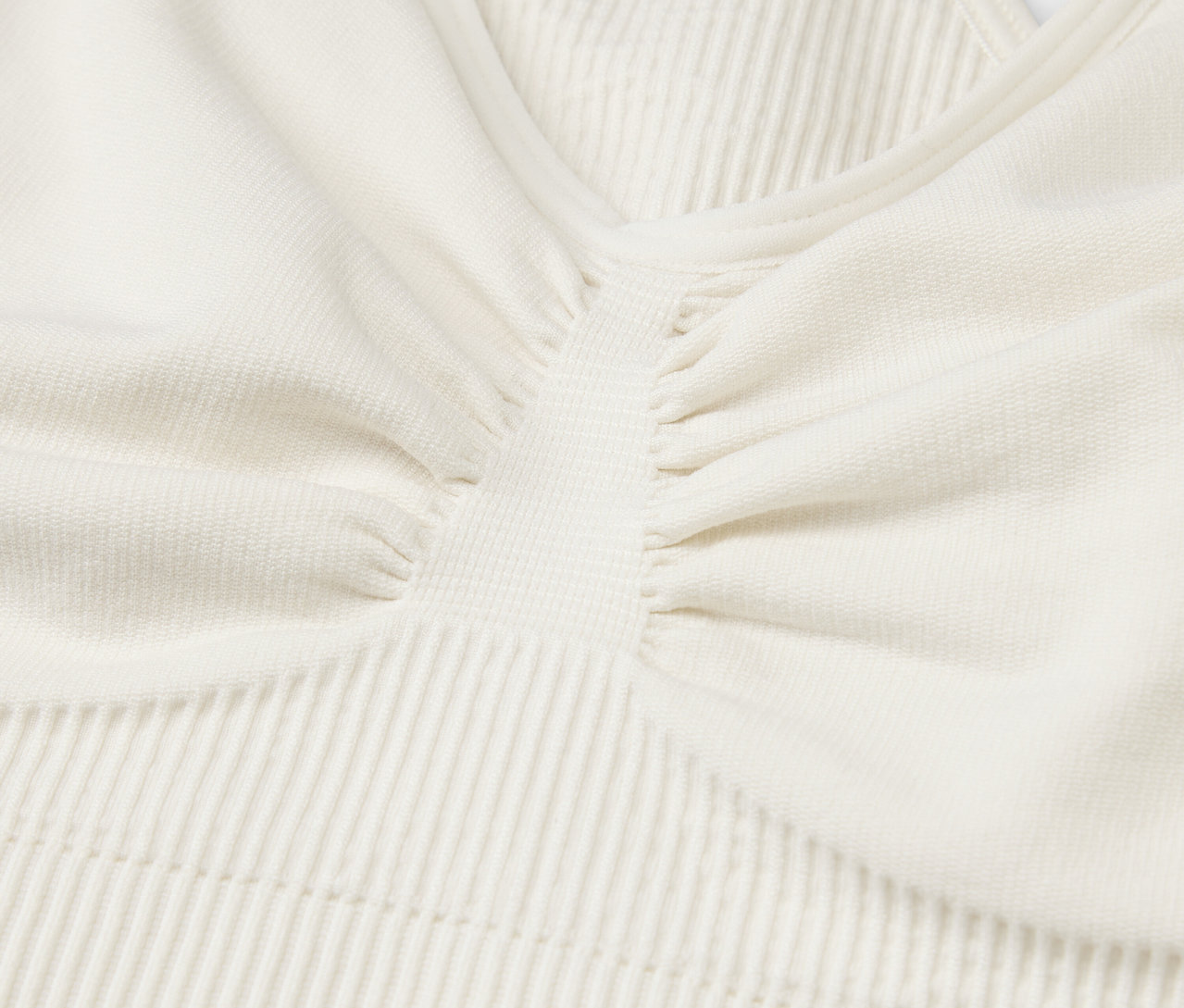 Zbliżenie na teksturowany materiał kremowego topu sportowego.