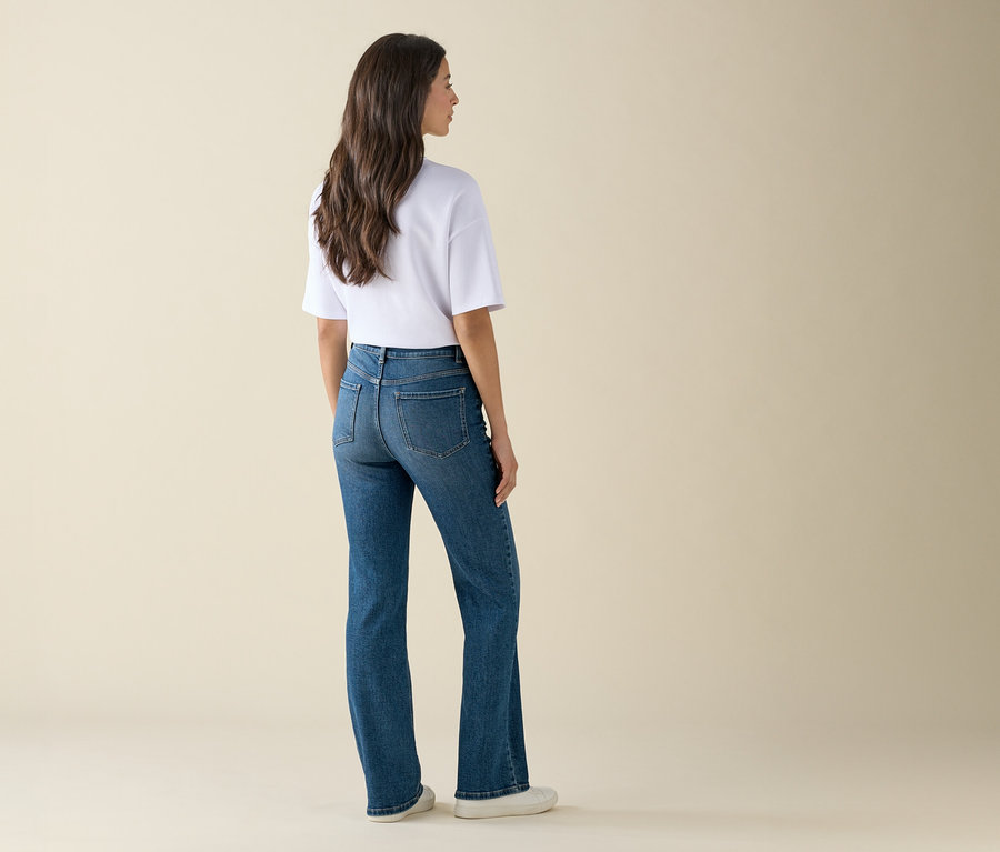 Kobieta stoi tyłem, ma na sobie niebieskie dżinsy i białą koszulkę.