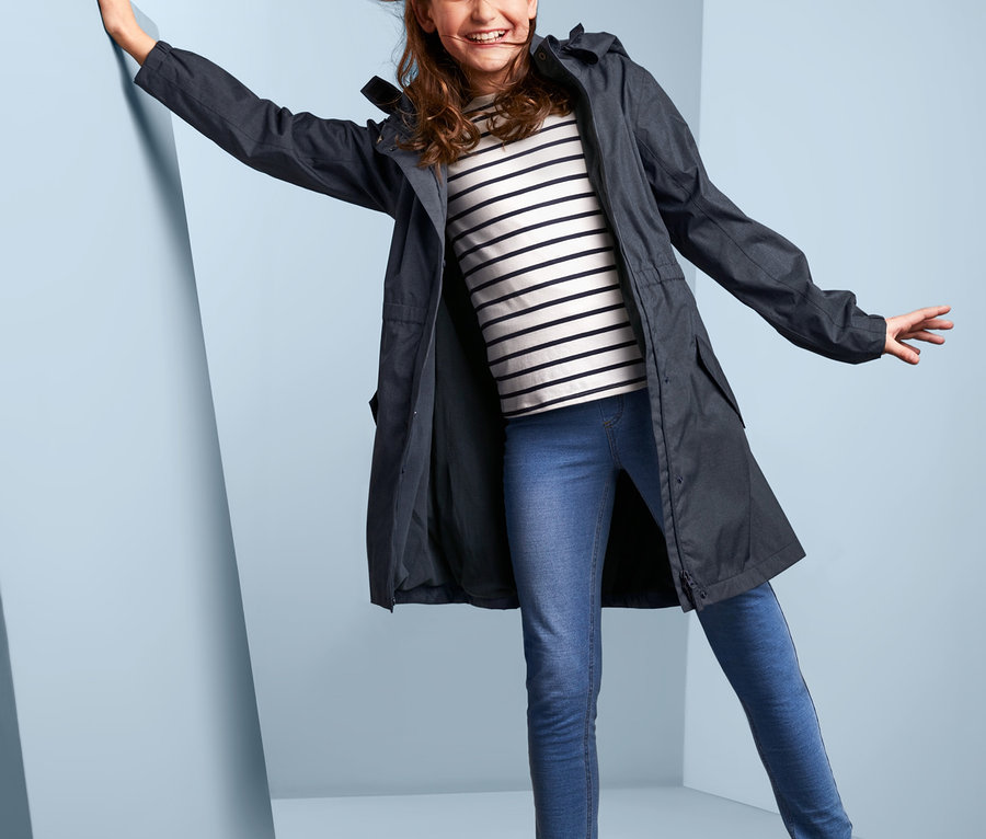 Dziewczyna pozuje w kurtce przeciwdeszczowej stylizowanej na dżins, bluzce w paski, dżinsach i kaloszach.