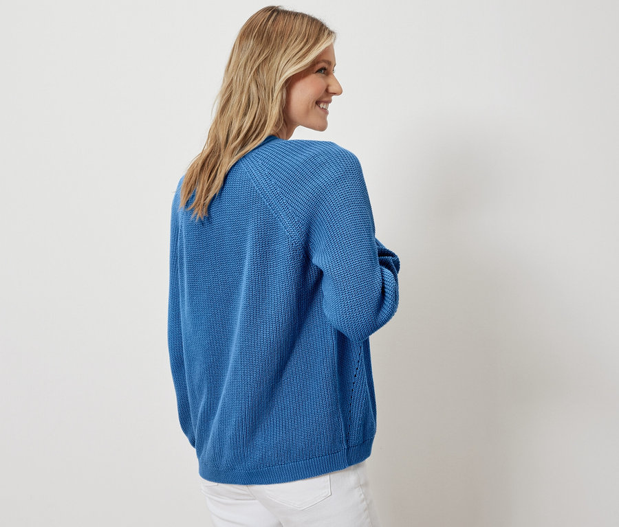 Kobieta pozuje w kardiganie i białych dżinsach.