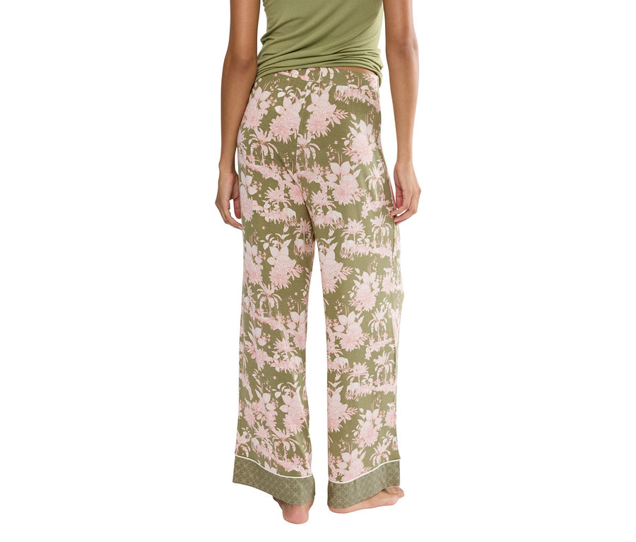 Widok z tyłu kobiety w zielonych spodniach w różowe kwiaty i zielonym topie.