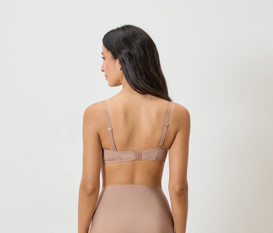 Widok z tyłu kobiety o ciemnych włosach w staniku i bieliźnie w kolorze nude.