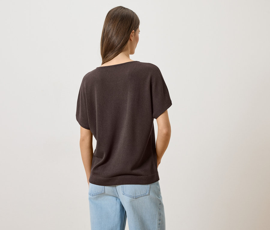 Widok z tyłu na kobietę z brązowymi włosami, ubraną w brązowy T-shirt i jasnoniebieskie dżinsy.