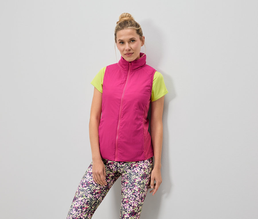 Kobieta ma na sobie różową kamizelkę nałożoną na jasnozielony T-shirt i legginsy w kwiaty.