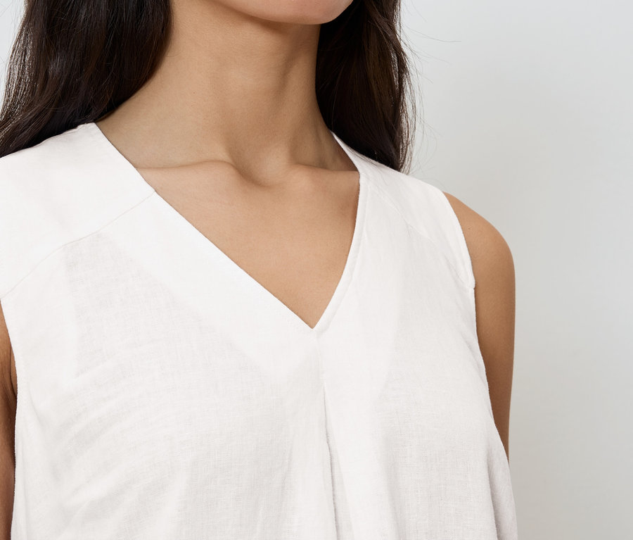 Zbliżenie kobiety ubranej w białą bluzkę bez rękawów z dekoltem w serek.