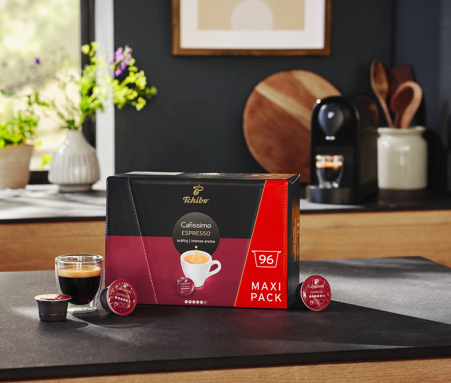 Czarny ekspres Cafissimo pure+ i opakowanie 96 kapsułek espresso na blacie.