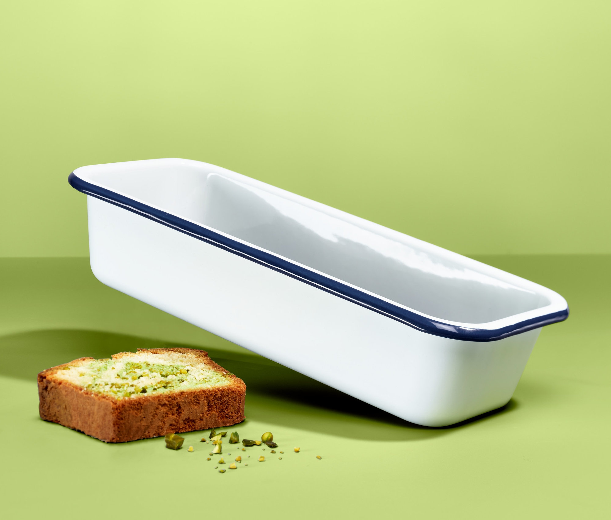 Unosząca się emaliowana forma do pieczenia obok kawałka ciasta na zielonym tle.