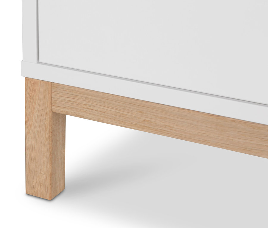 Szczegół białej szafy na ubrania »Eklund« z szufladami i drewnianymi nóżkami.