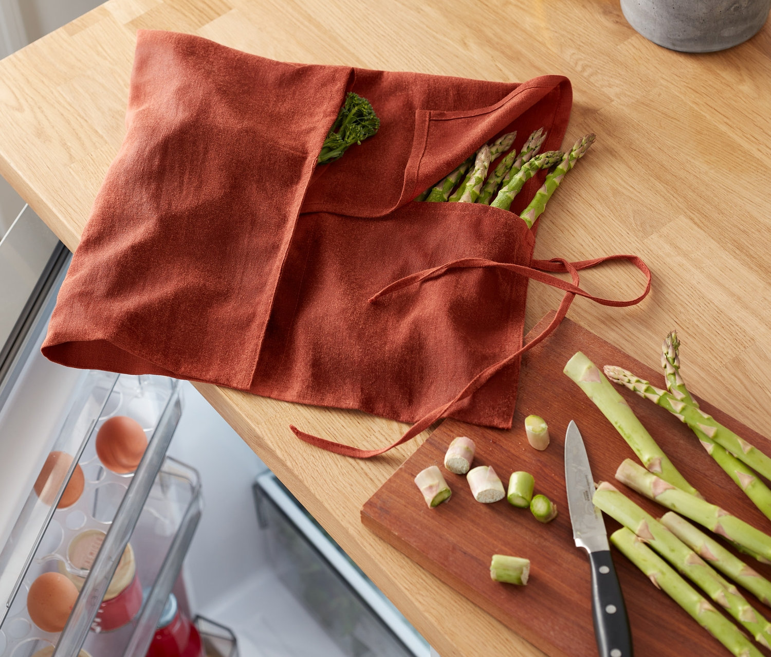 Na lnianej ściereczce do warzyw leżą zielone szparagi obok pokrojonych warzyw i noża.