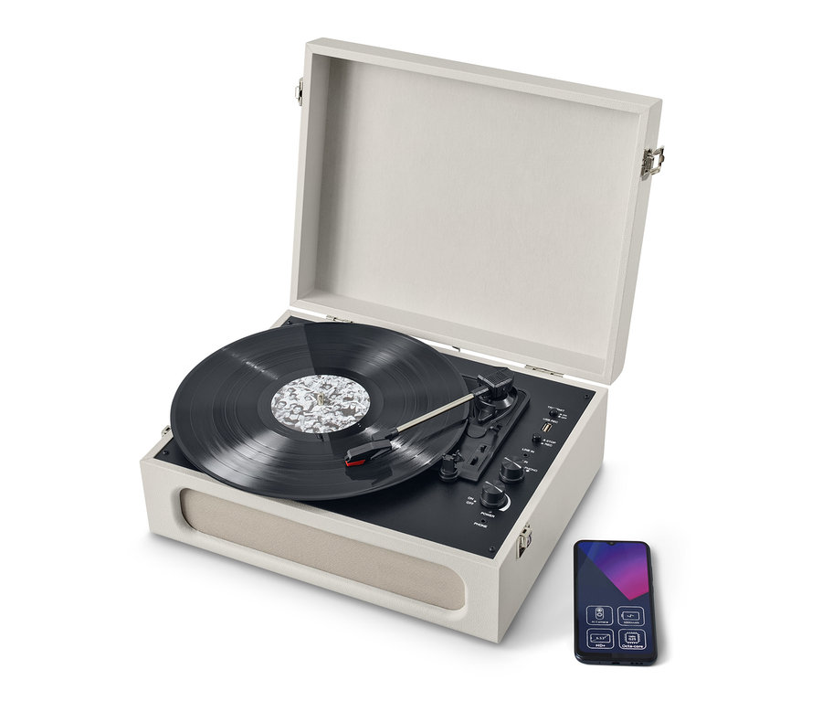 Beżowy, przenośny gramofon retro z funkcją Bluetooth® z otwartą pokrywą i płytą. Obok gramofonu znajduje się smartfon.