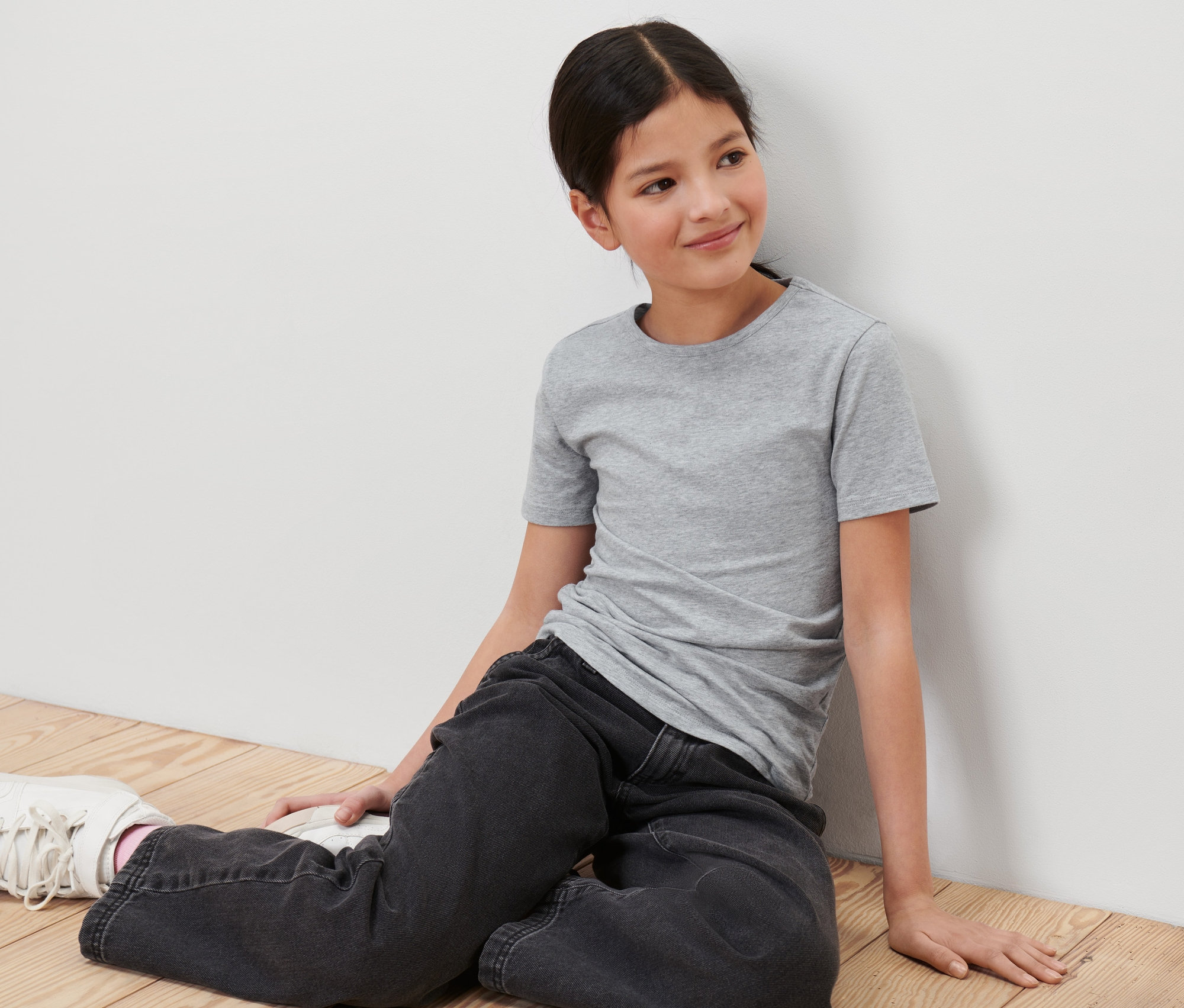 Dziewczyna siedzi na podłodze i ma na sobie szarą koszulkę z Koszulki dziecięce, 3 sztuki.
