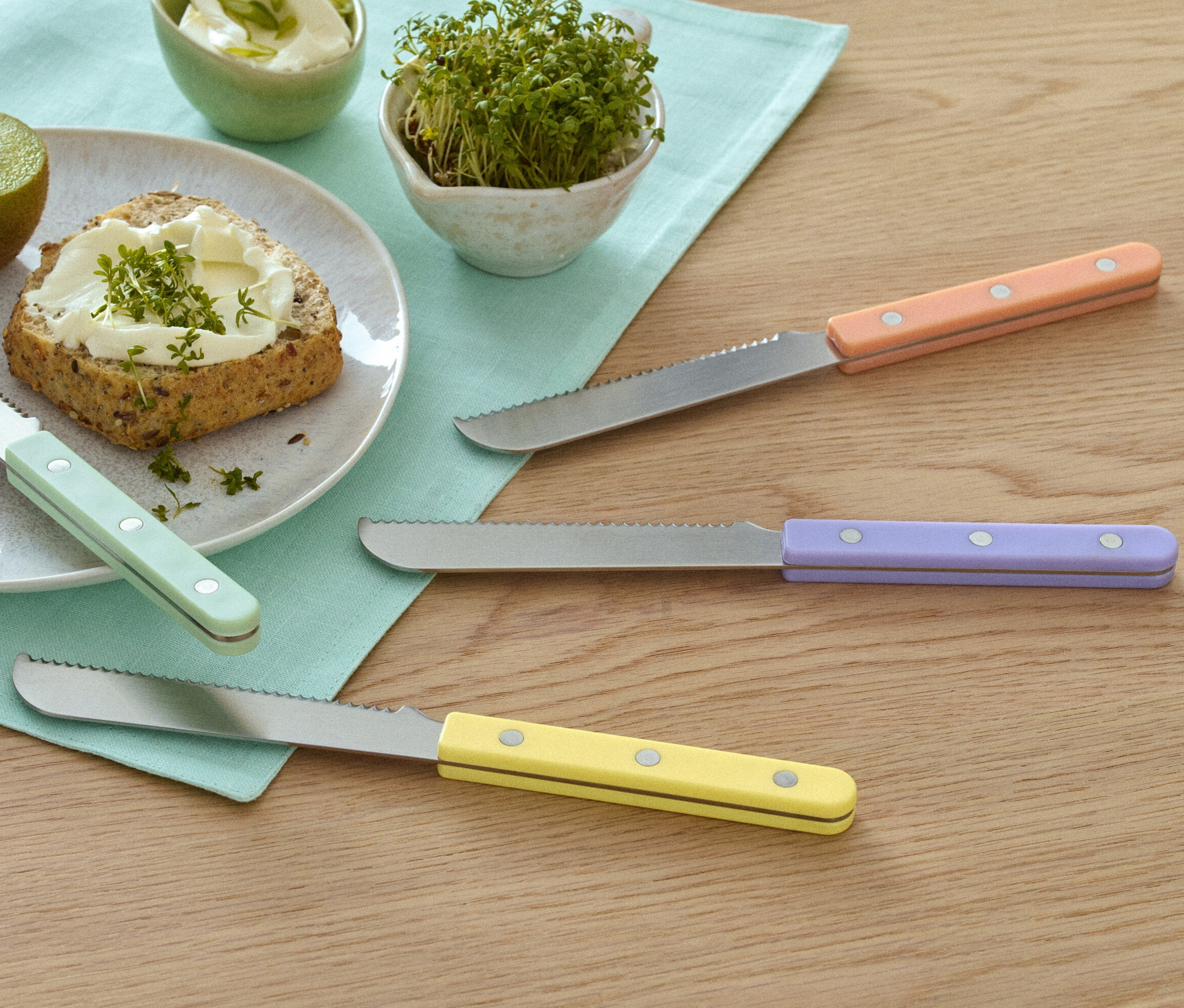 Talerz z kiwi, chlebem z pastą i rzeżuchą obok 4 noży śniadaniowych.