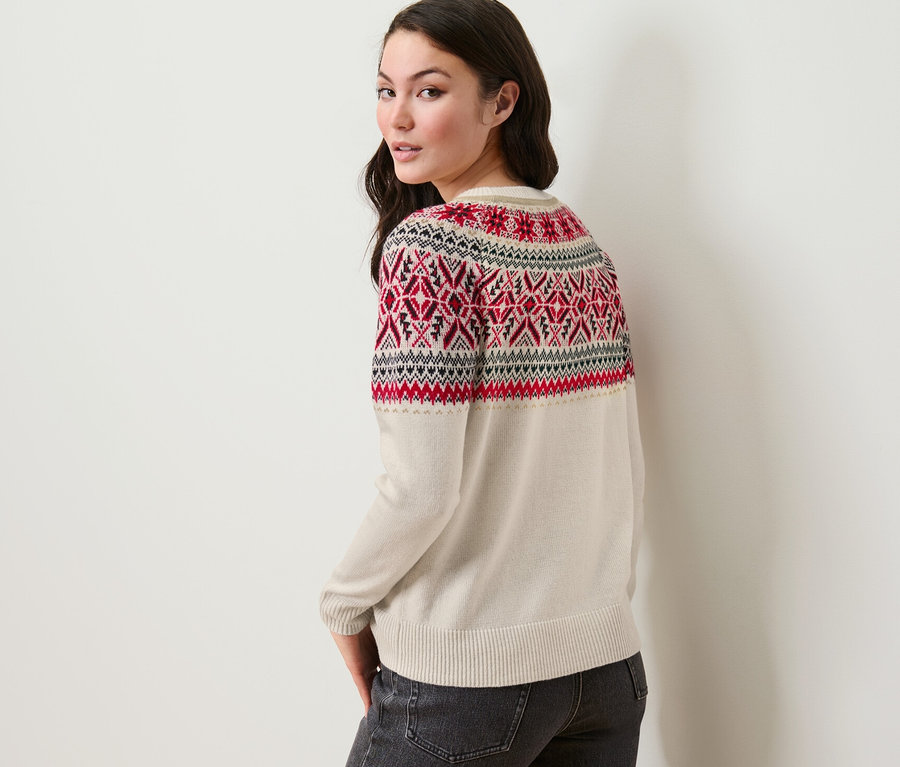 Kobieta patrzy przez ramię, ubrana w sweter z norweskim wzorem i dżinsy.