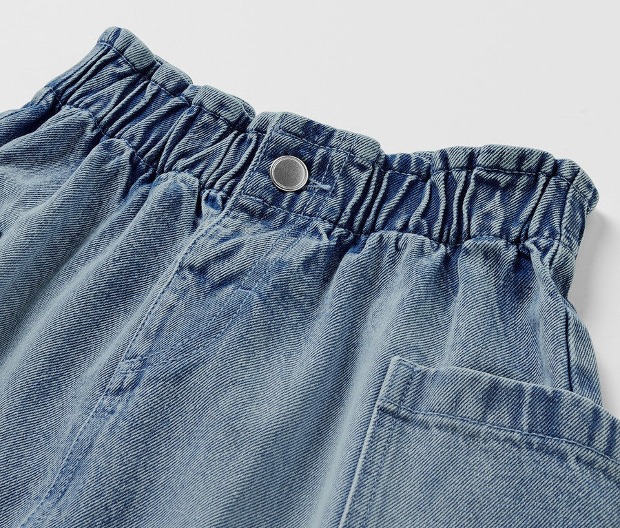 Zbliżenie na dżinsową spódnicę typu paperbag z zapięciem na guzik i kieszeniami.