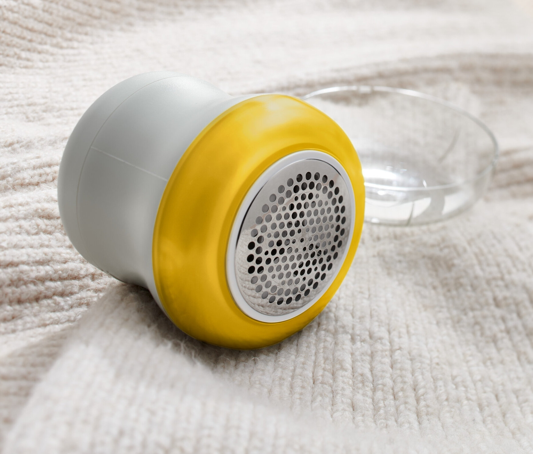 Szara golarka do odzieży leży na jasnym wełnianym swetrze.