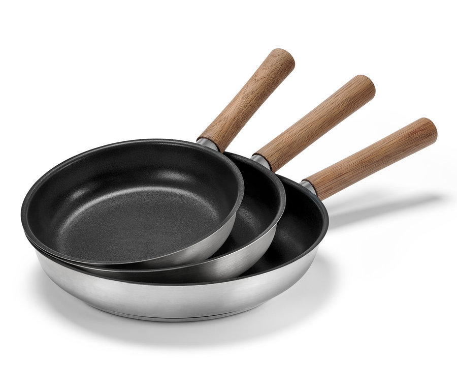 Trzy patelnie ze stali nierdzewnej z drewnianymi rączkami o średnicy 20, 24 i 28 cm ułożone jedna na drugiej.