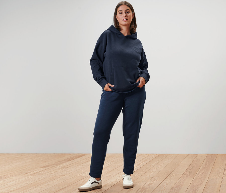 Kobieta pozuje w granatowej bluzie z kapturem, spodniach dresowych i skórzanych sneakersach.