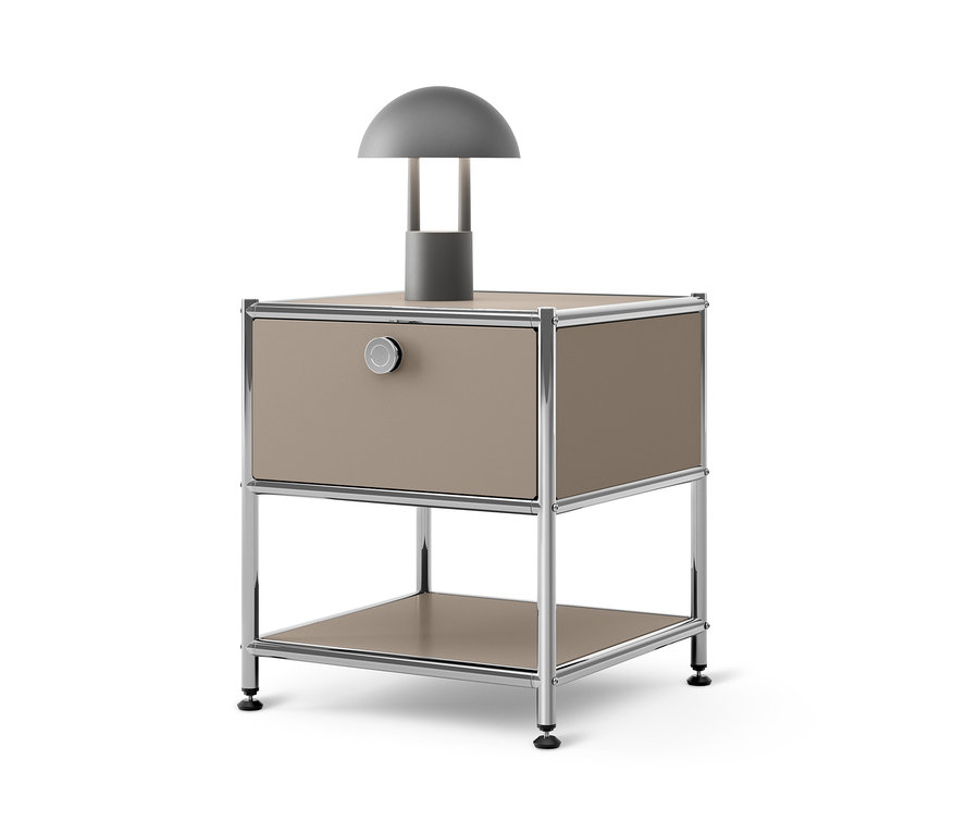 Szara lampa stoi na beżowym metalowym stoliku z szufladą »CN3«.