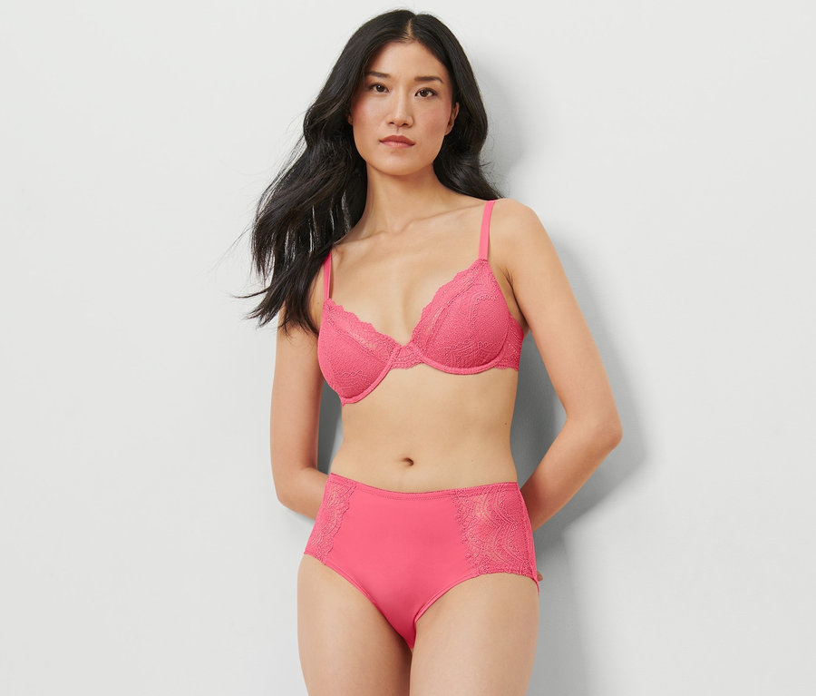 Kobieta pozuje w studio w różowym biustonoszu i figach ze średnim stanem.