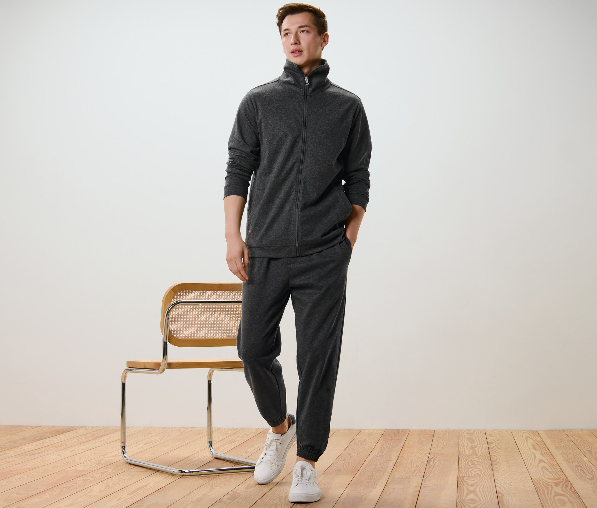 Mężczyzna pozuje w zestawie ubrań domowych i białych tenisówkach obok krzesła.