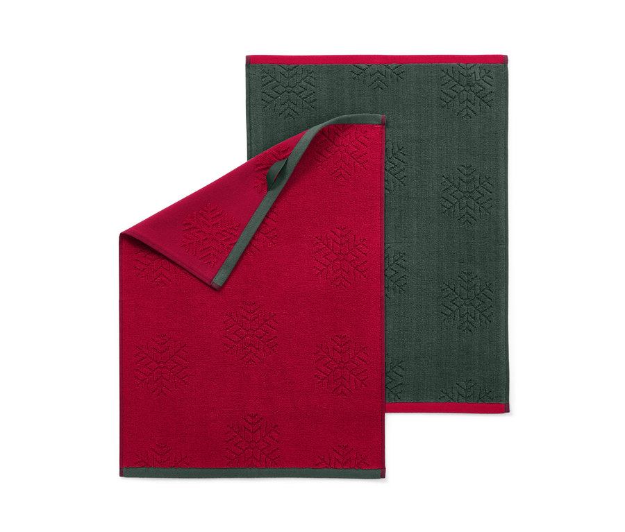 Dwa ręczniki kuchenne we wzór płatków śniegu, jeden czerwony i jeden ciemnozielony.