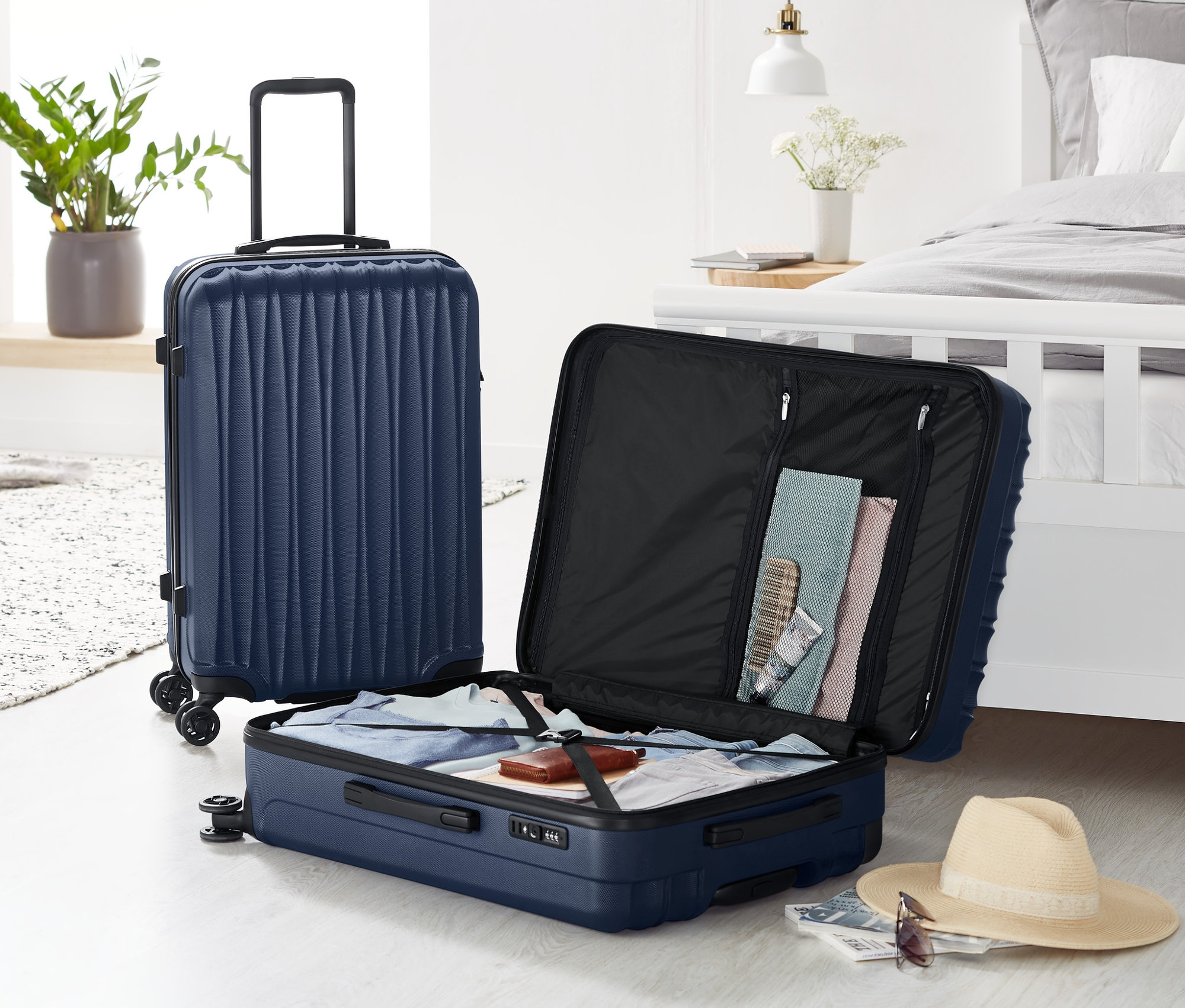 Dwa komplety twardych walizek: jeden duży stoi, jeden mały jest otwarty i wypełniony ubraniami.