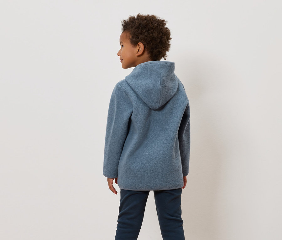 Chłopiec o kręconych włosach ma na sobie niebieską bluzę z kapturem i granatowe spodnie.