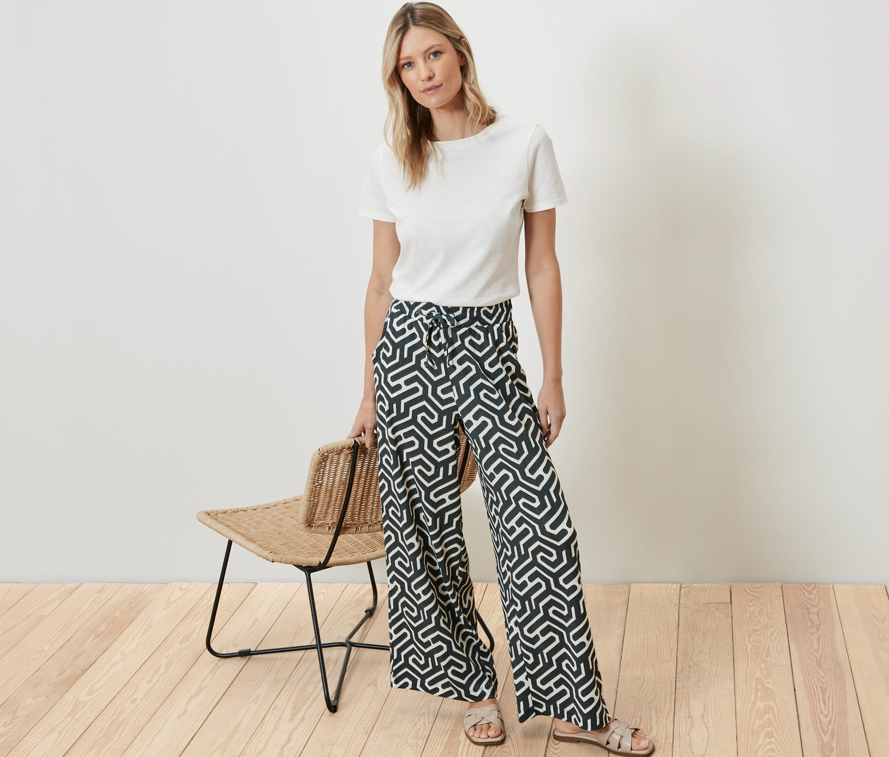 Kobieta stoi w białym T-shircie i spodniach na gumce z nadrukiem i efektem marszczenia.